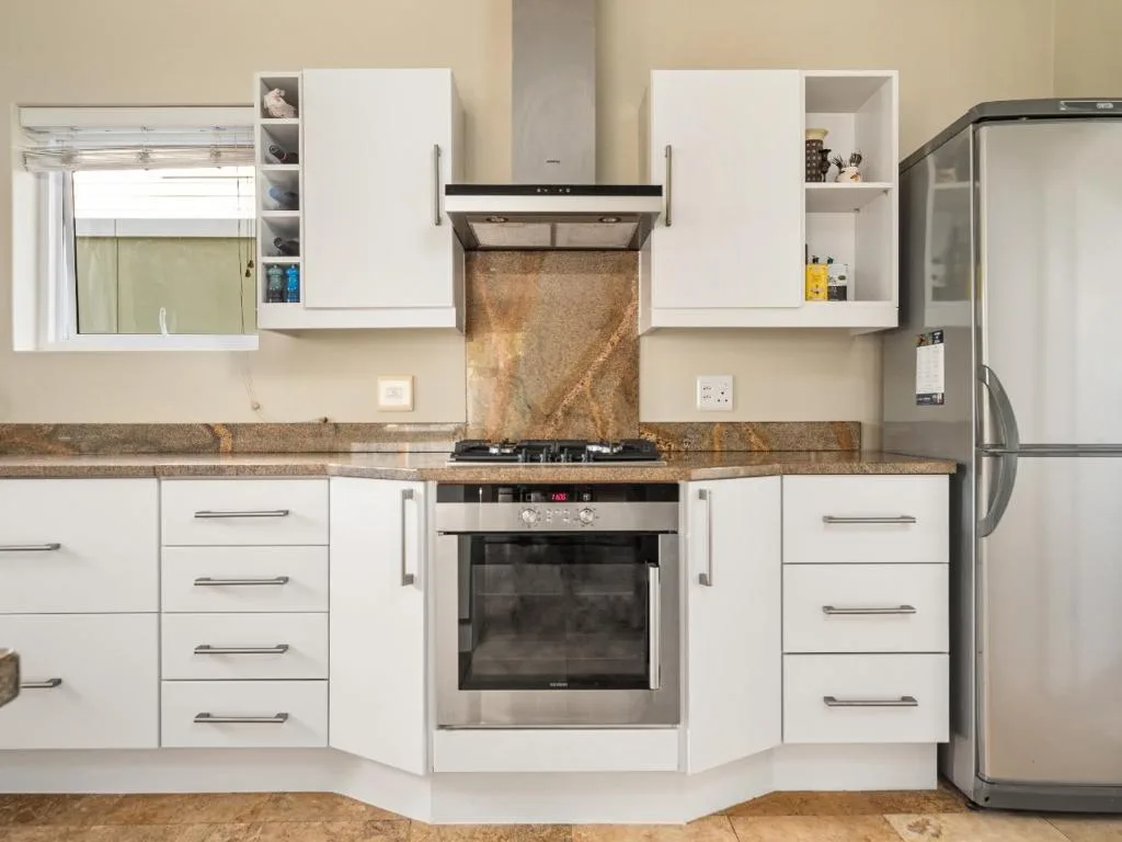 Modern white kitchen with granite countertop, stainless steel appliances, and storage cabinets