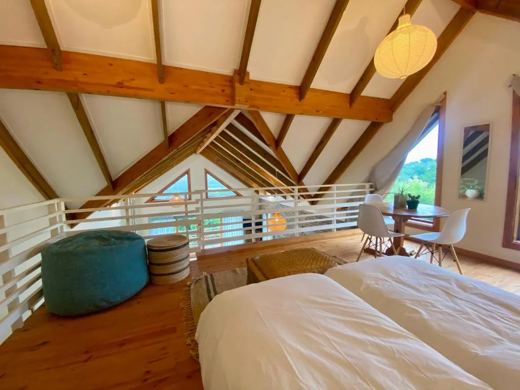 Spacious loft bedroom with exposed wooden beams and mezzanine railing overlooking views