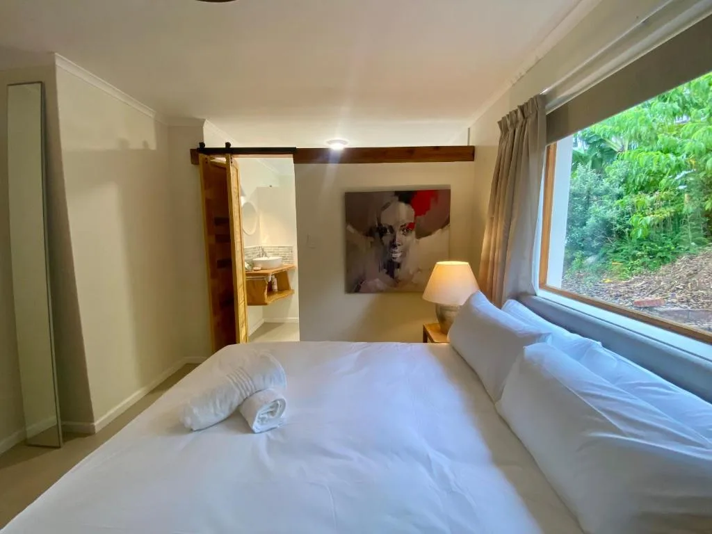 Bright bedroom with white bed, ensuite bathroom access, and garden views