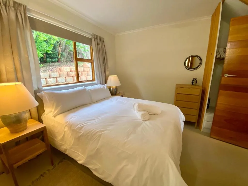 Bright bedroom with queen bed, white linens, wooden furniture, and garden view window