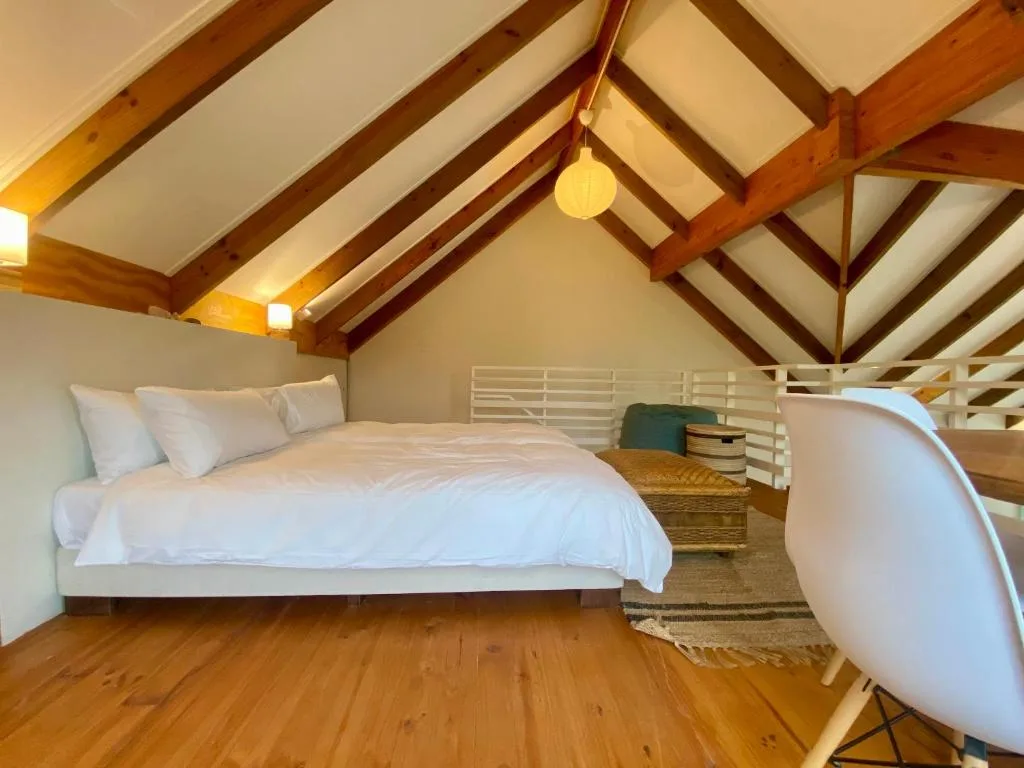 Loft bedroom with exposed wooden beams, white bedding, and wooden floors