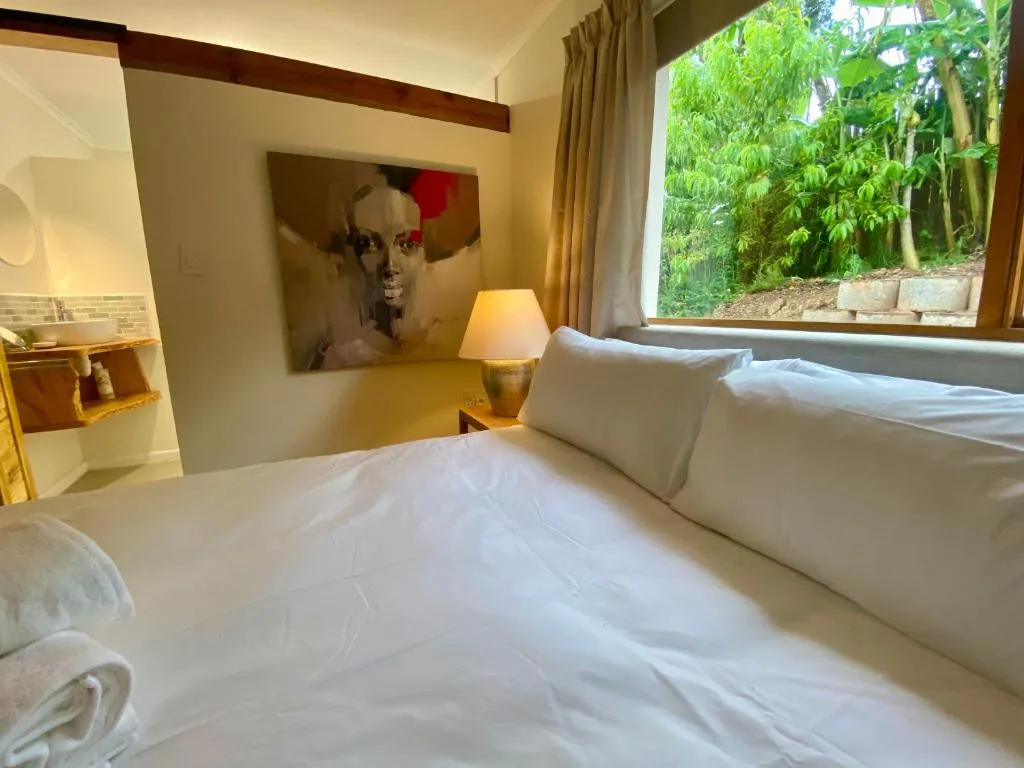 Bright bedroom with white bed, modern art, and garden views through large window