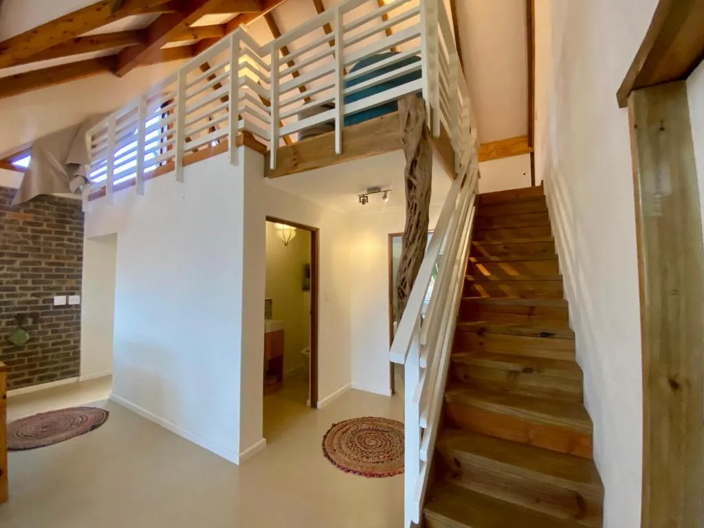 Interior staircase with wooden steps, white railings, and loft mezzanine above
