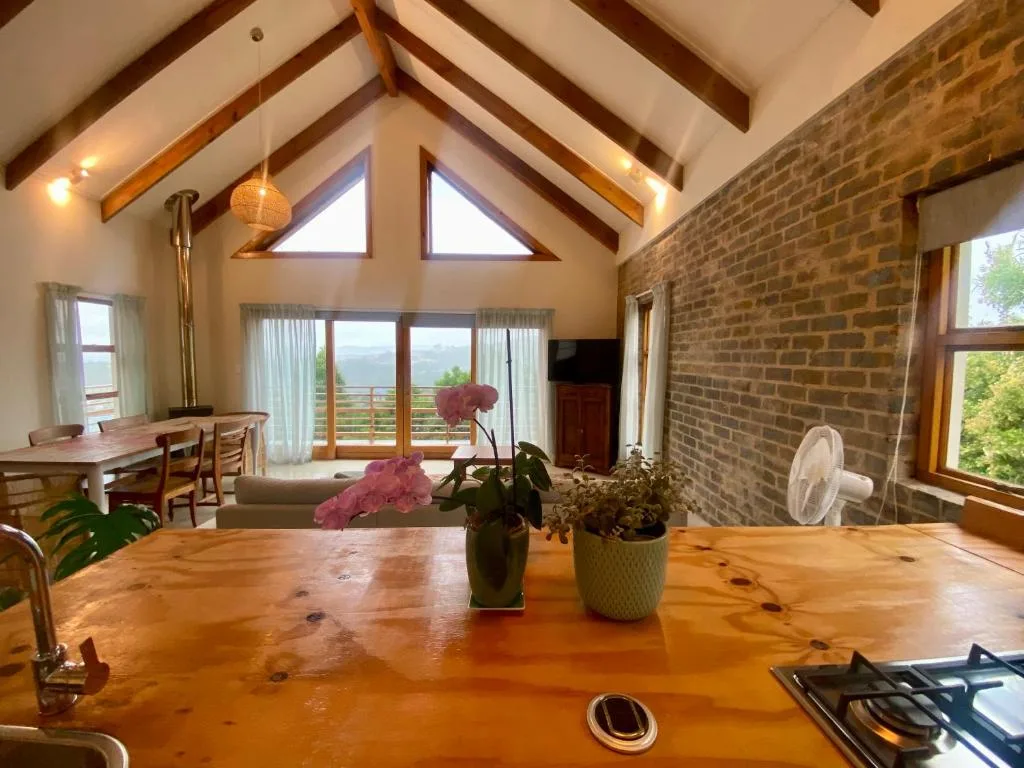 Open-plan lounge with wooden beams, brick accent wall, and mountain views