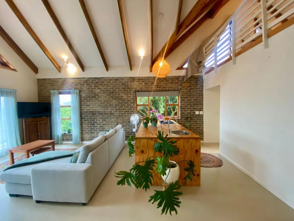 Spacious open-plan lounge with exposed beams, brick feature wall, and comfortable seating