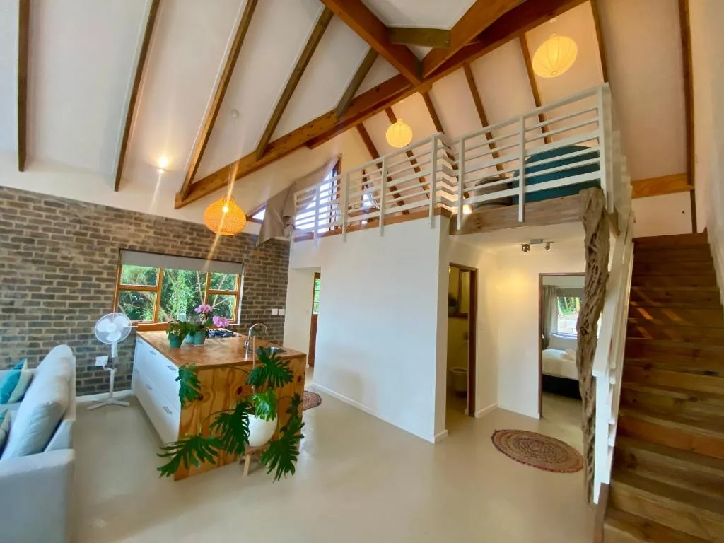 Open-plan lounge with exposed wooden beams, mezzanine level, and brick accent wall