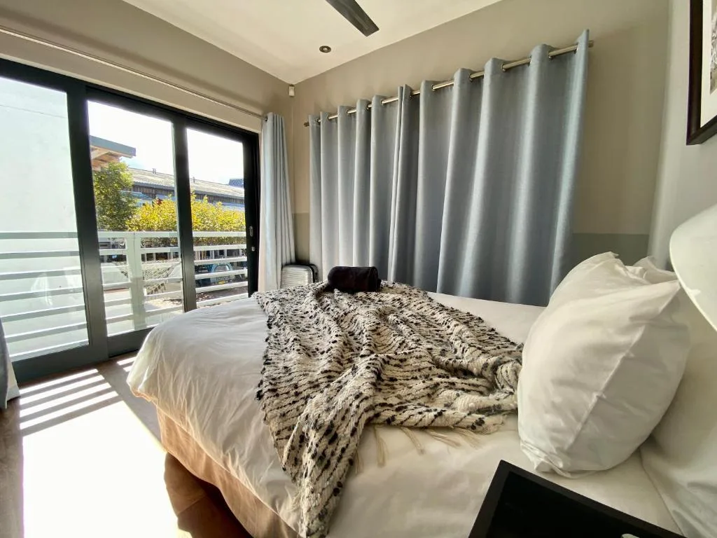 Modern bedroom with queen bed, patterned throw, and glass doors overlooking balcony
