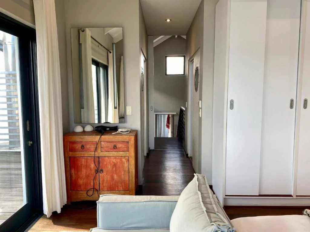 Modern bedroom with wooden dresser, mirror, and built-in wardrobes along hallway