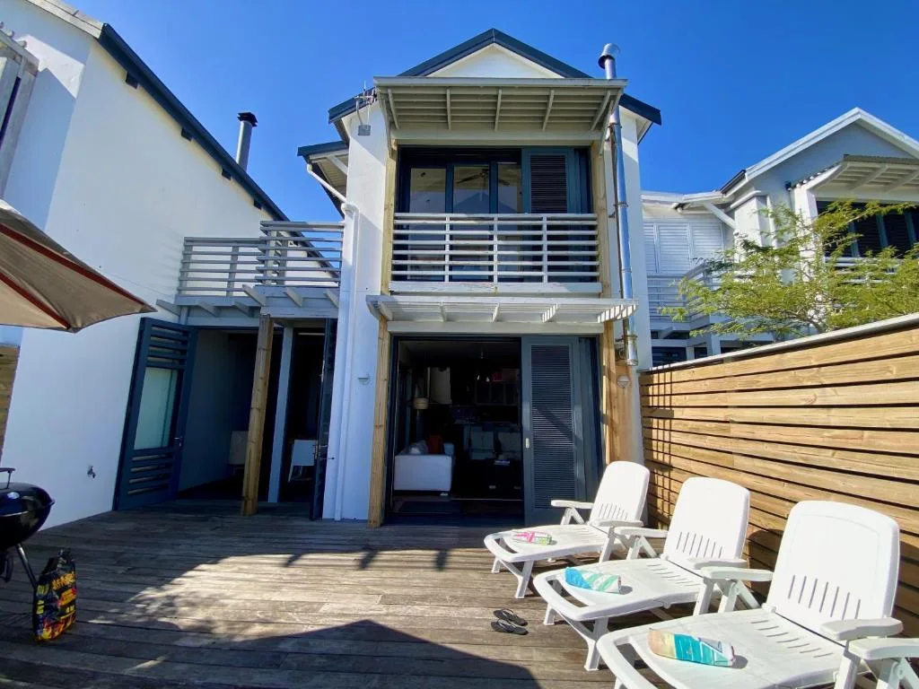Spacious wooden deck with white loungers and coastal home facade