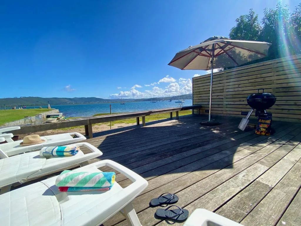 Wooden deck with lounge chairs, umbrella, and braai overlooking bay