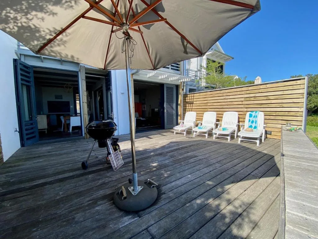 Spacious wooden deck with umbrella, loungers, braai grill, and wooden privacy screen