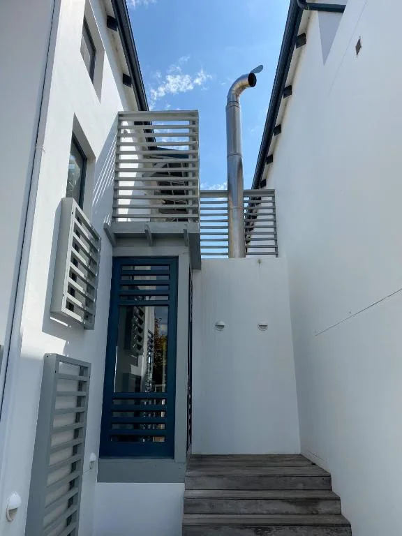 Modern white townhouse entrance with blue door and wooden deck stairs