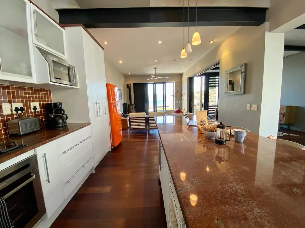 Modern open-plan kitchen with white cabinetry, orange fridge, and brown countertops