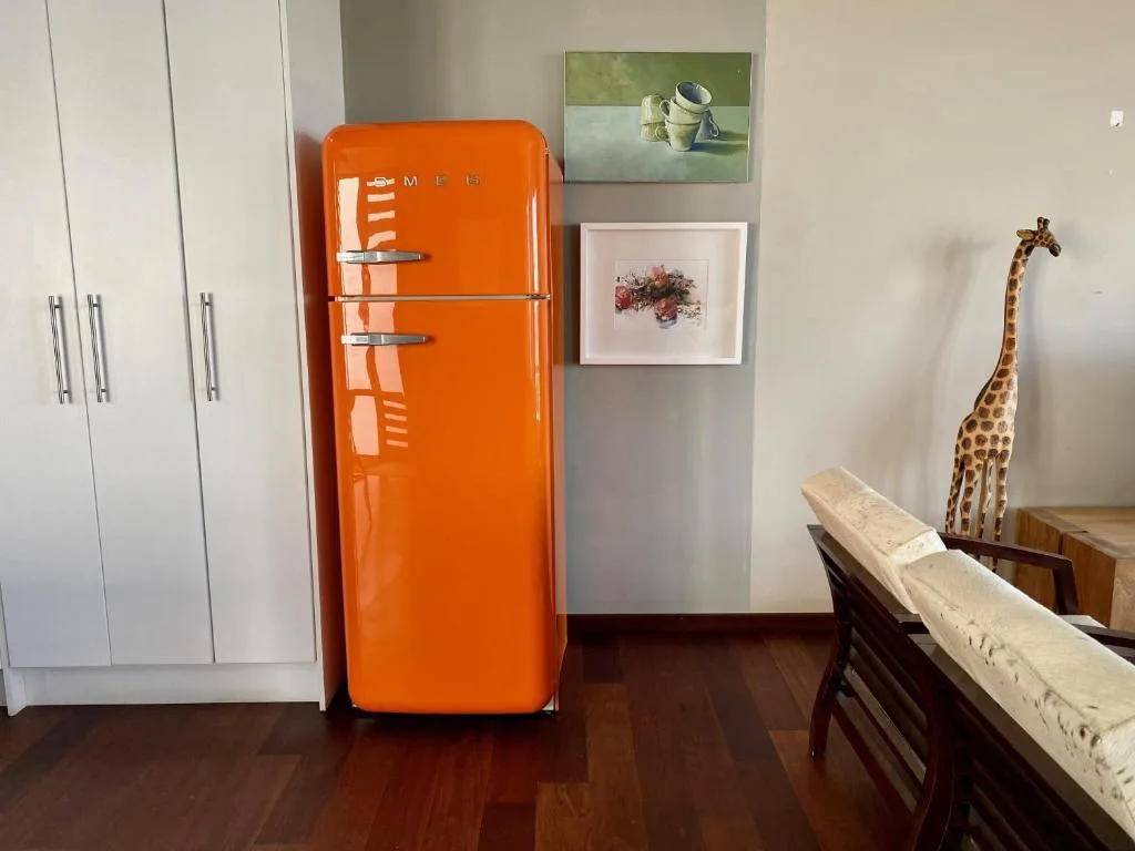 Modern kitchen with bright orange SMEG refrigerator and white cabinetry