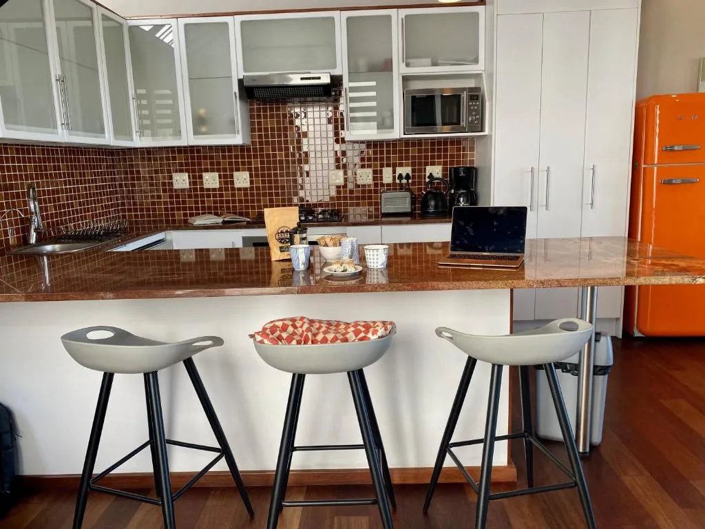 Modern kitchen with red tile backsplash, white cabinetry, and orange retro fridge