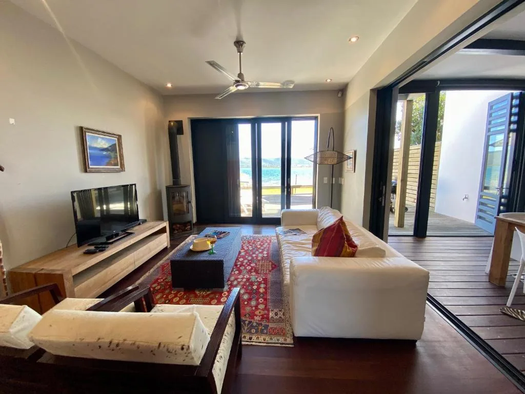 Spacious living room with cream sofas, TV, and ocean views through glass doors