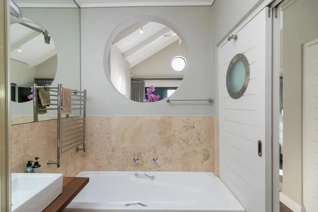 Modern bathroom with curved mirror, soaking tub, and heated towel rail