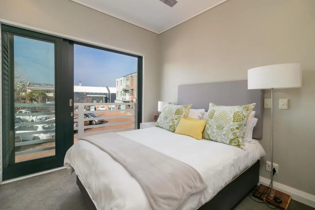 Modern bedroom with queen bed, green accent pillows, and sliding glass doors to deck