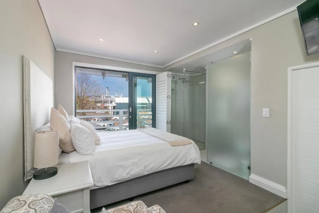 Modern bedroom with white bedding, large window overlooking Knysna harbor
