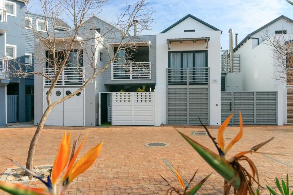 Modern white townhouses with metal railings and garage doors on brick driveway