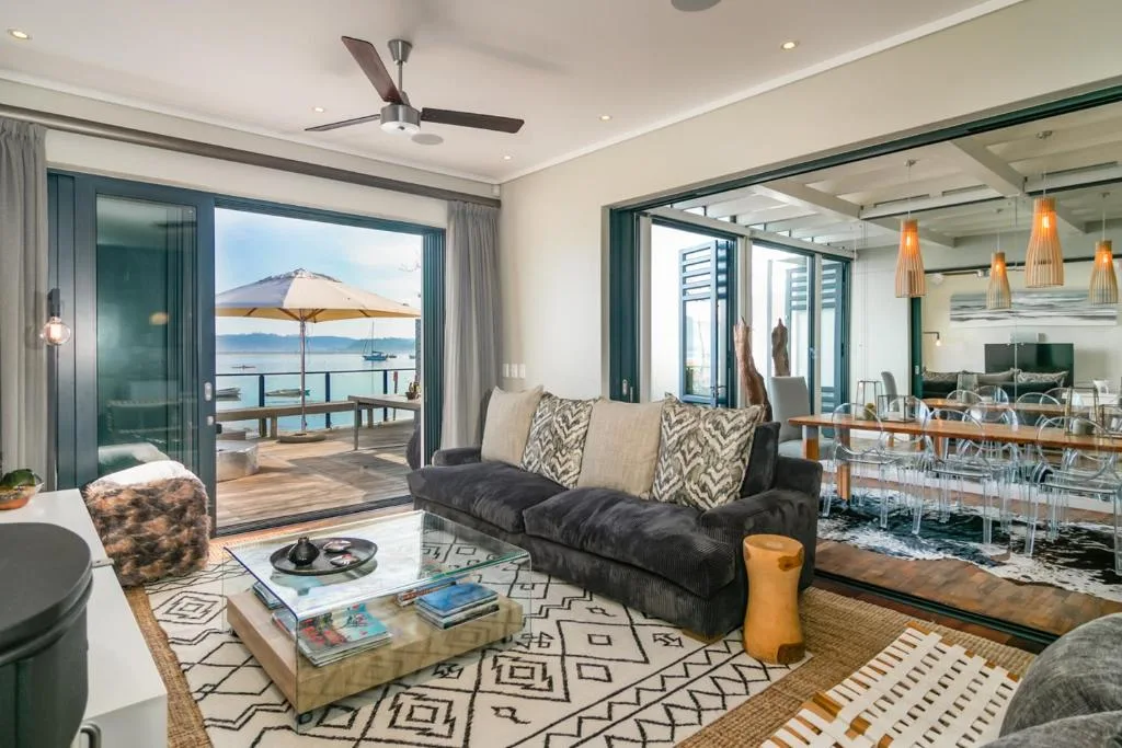 Modern lounge with black sofa, ocean view through sliding doors, ceiling fan