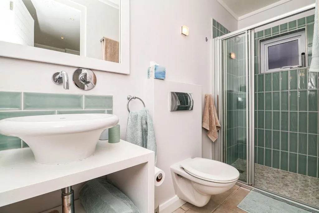 Modern bathroom with round sink, green tile shower enclosure, and wall-mounted fixtures