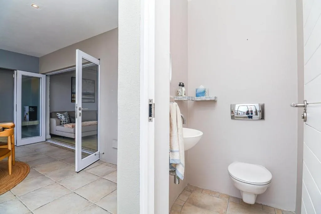 Compact ensuite bathroom with toilet, wall-mounted shelf, and neutral tiled walls