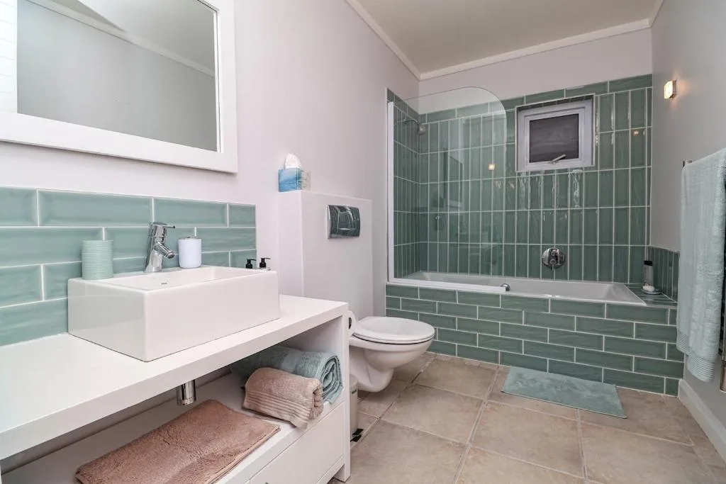 Modern bathroom with green tiled shower, vanity sink, and toilet