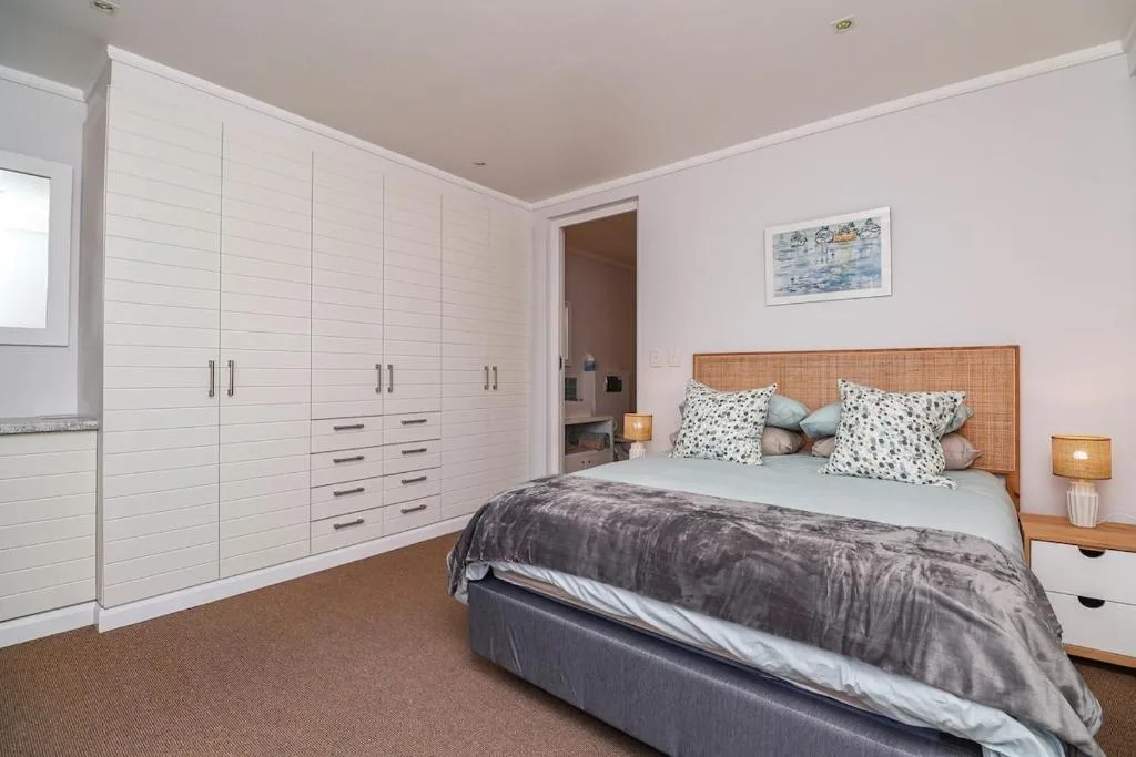 Spacious bedroom with queen bed, rattan headboard, and built-in white wardrobes