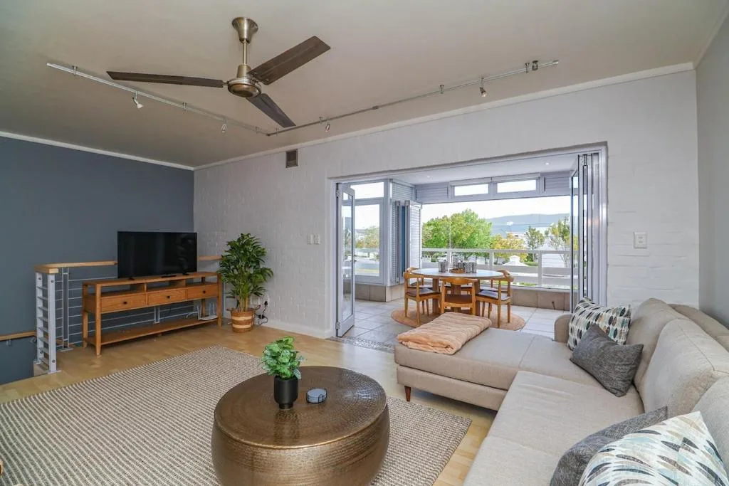 Modern lounge with cream sectional sofa, wooden coffee table, and ocean views through glass doors