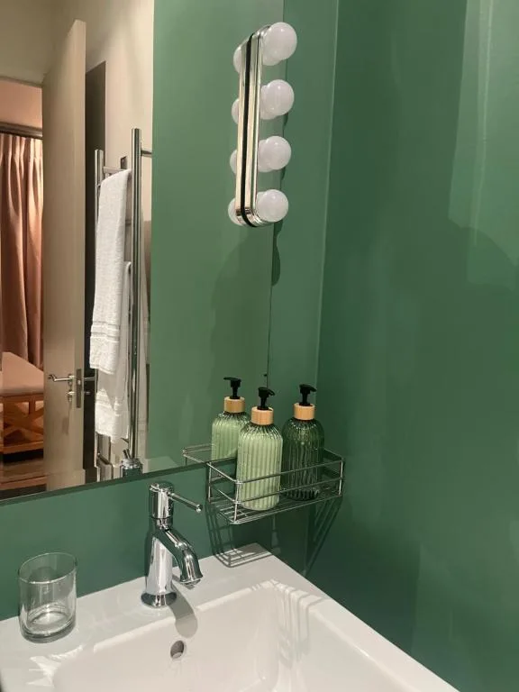 Modern bathroom vanity with green walls, illuminated mirror, and amenities shelf