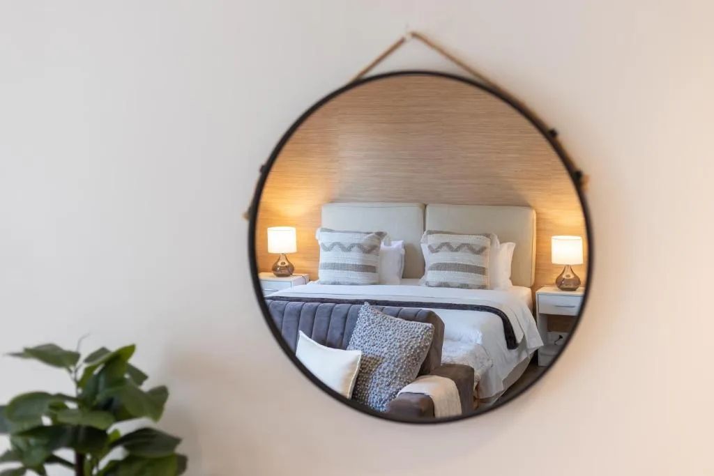 Bedroom reflected in round mirror with bed, pillows, and bedside lamps