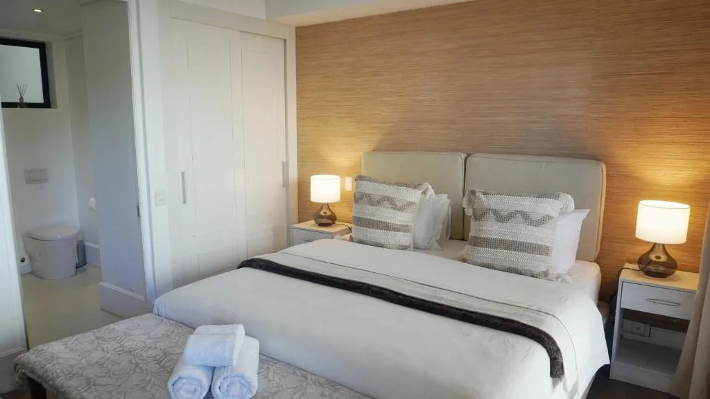 Modern bedroom with double bed, warm wood accent wall, and ensuite bathroom