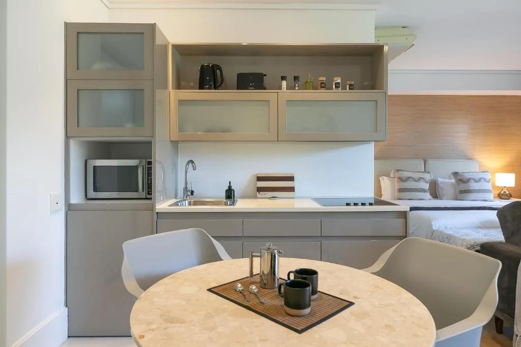 Modern kitchen with gray cabinetry, sink, microwave, and open shelving displaying amenities