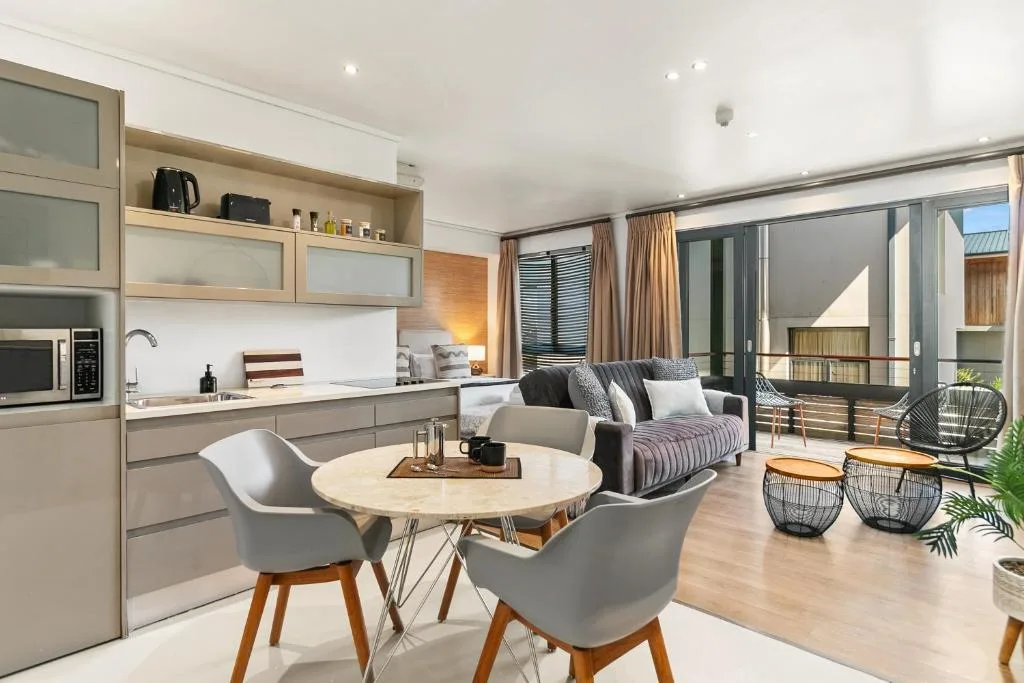 Open-plan living area with sofa, round dining table, and modern kitchen overlooking deck