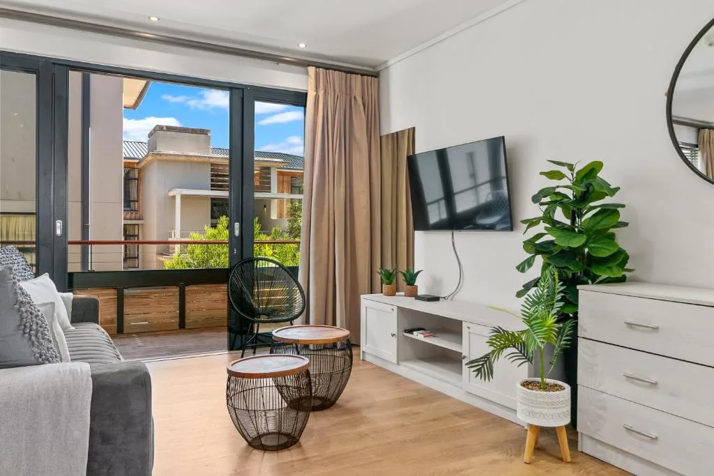 Modern lounge with sofa, TV, and access to deck with garden views