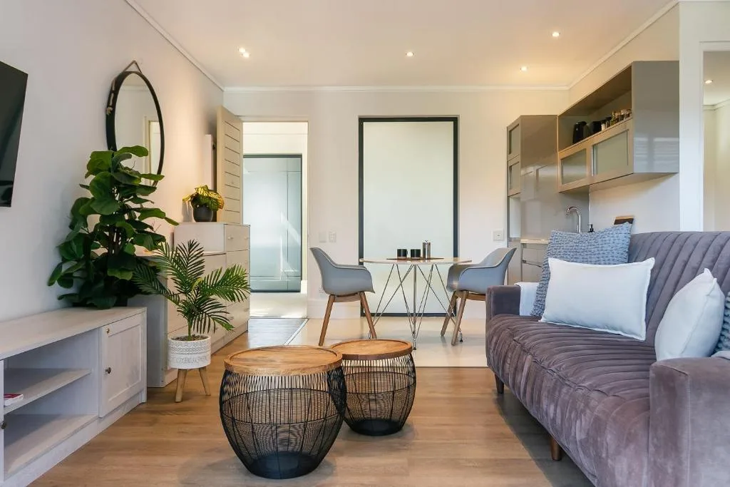 Modern lounge with gray sofa, woven poufs, plants, and open-plan kitchen