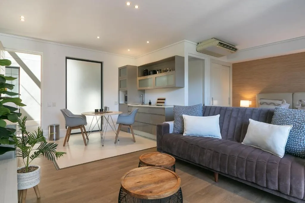 Modern lounge with grey sofa, wooden coffee tables, and kitchenette visible