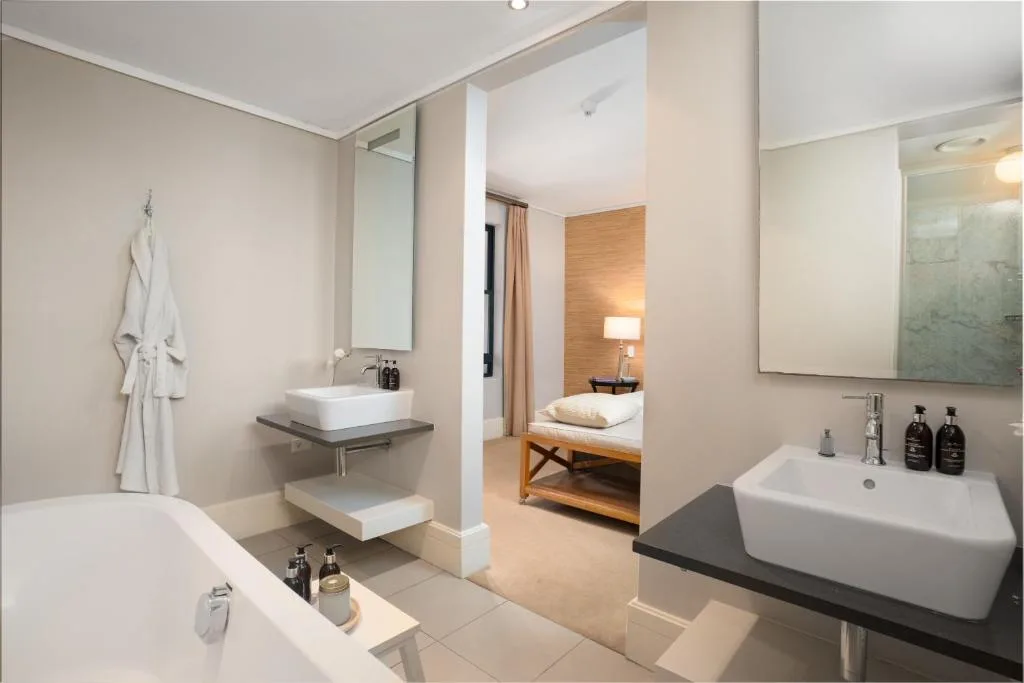 Modern bathroom with dual vanities, soaking tub, and view to bedroom