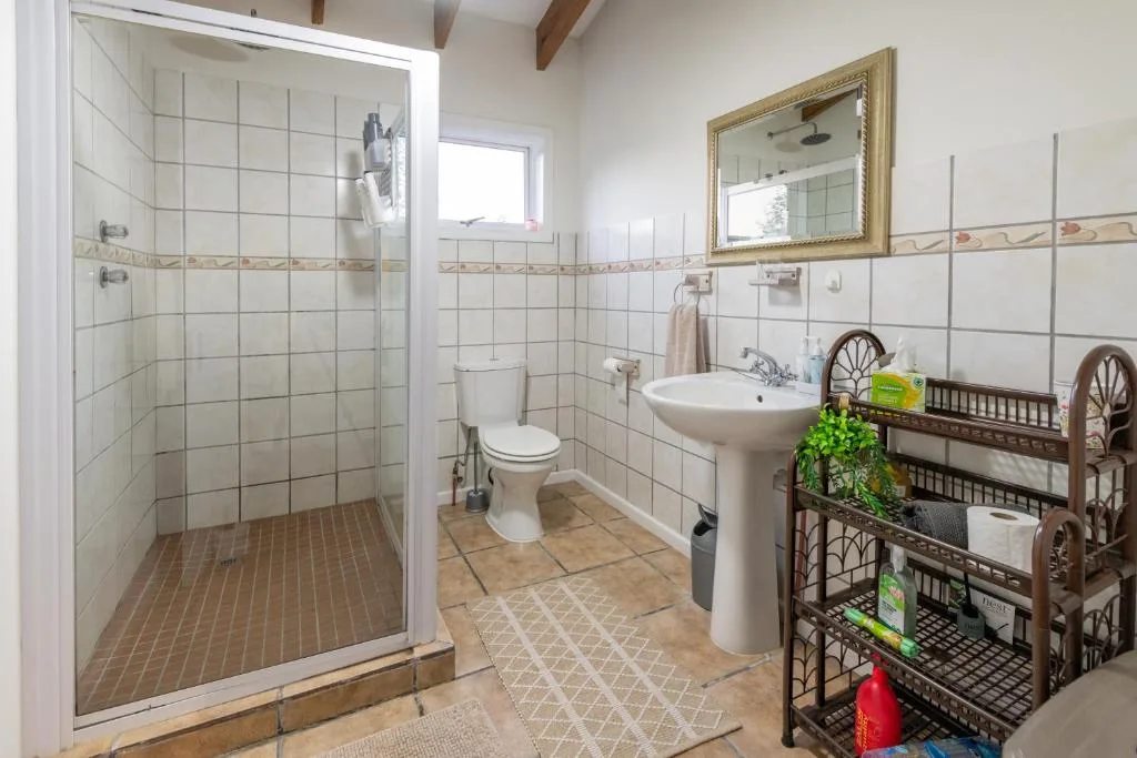 Spacious bathroom with walk-in shower, pedestal sink, and storage shelves