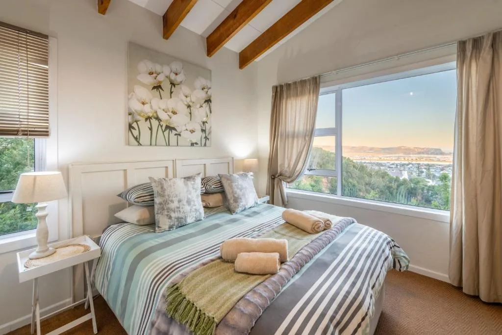 Bright bedroom with striped bedding, wooden beams, scenic lagoon view windows