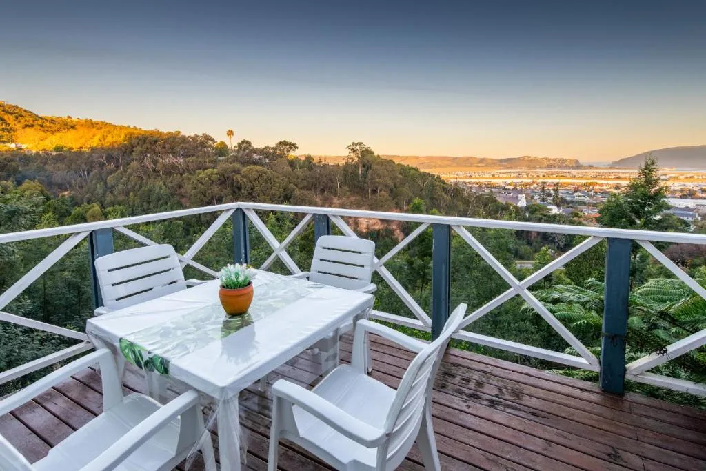 Elevated deck with dining table overlooking lush forest and distant lagoon at sunset