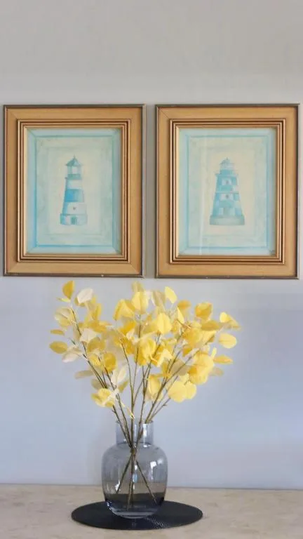 Framed lighthouse artwork above yellow flowers in glass vase