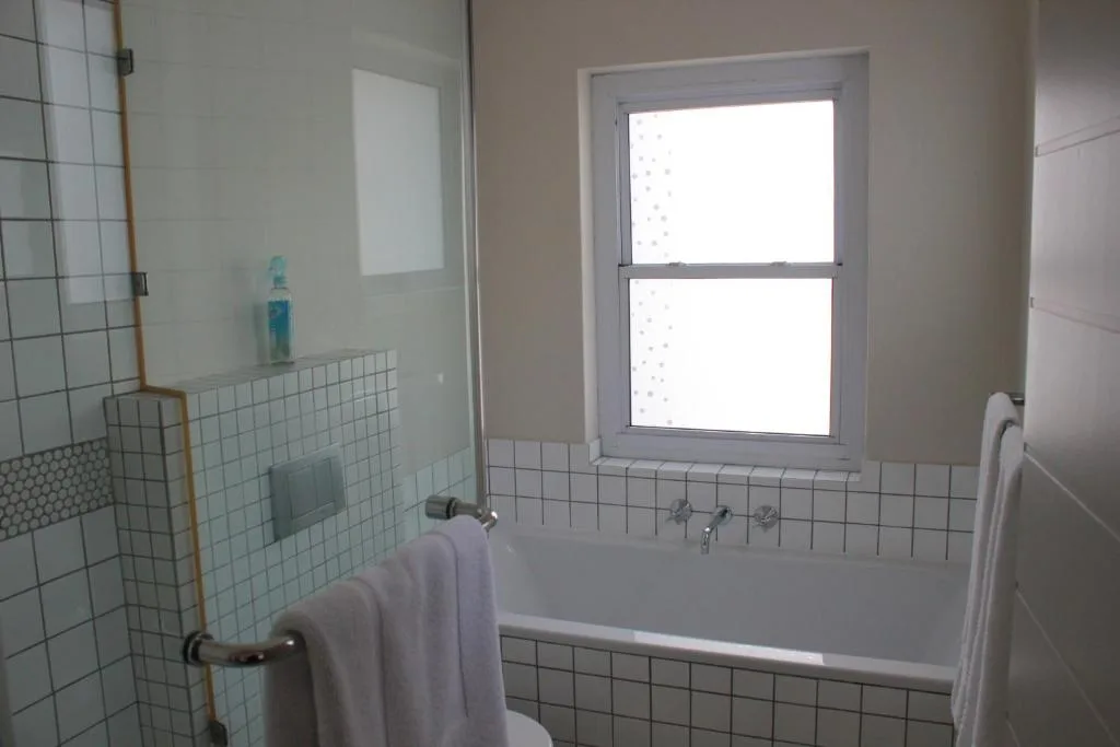 Bright bathroom with tiled walls, bathtub, and window overlooking garden