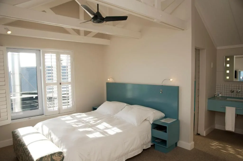 Bright bedroom with queen bed, teal headboard, ceiling fan, and ocean views