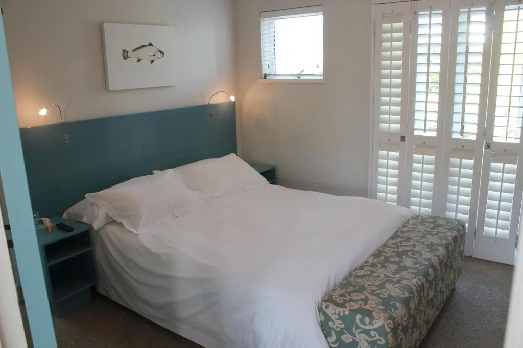 Bright bedroom with teal headboard, white bedding, coastal artwork above bed