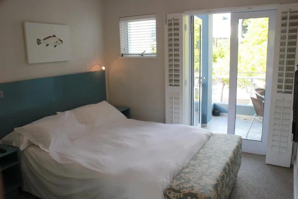 Bright bedroom with teal headboard, white linens, and deck access