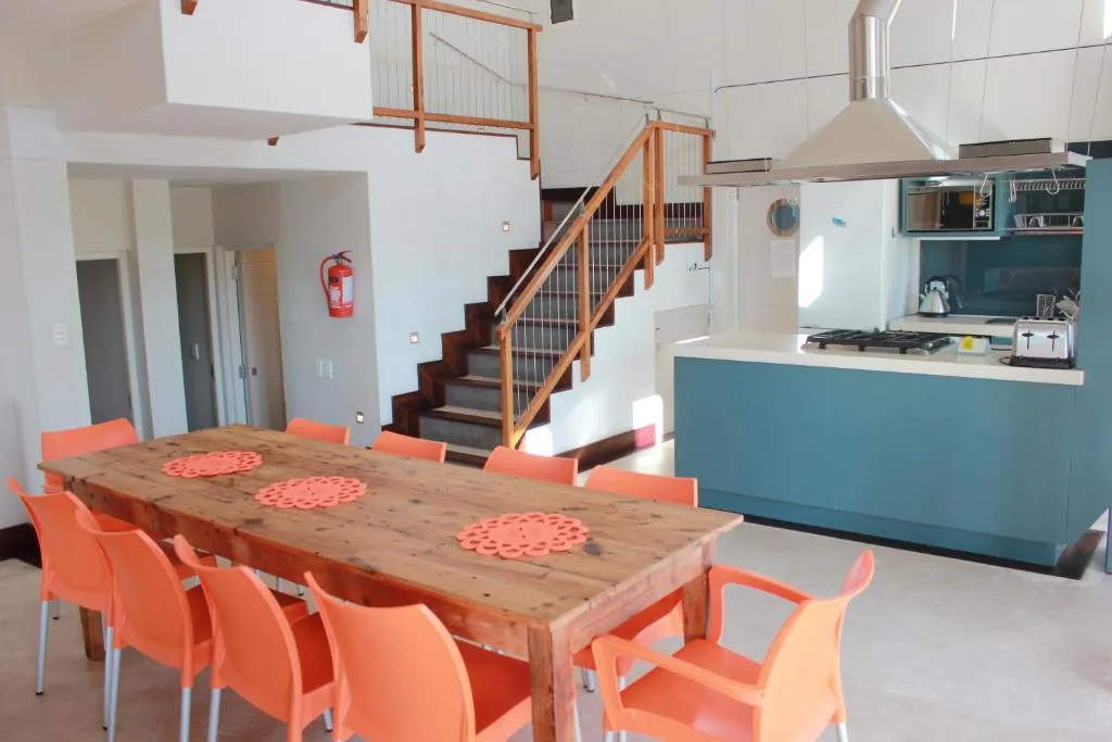 Open-plan dining area with wooden table and orange chairs, adjacent kitchen
