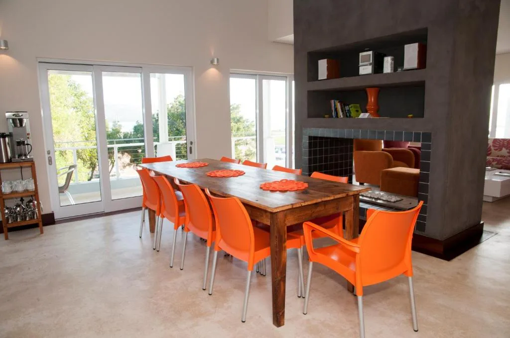 Modern dining area with wooden table and bright orange chairs overlooking garden views