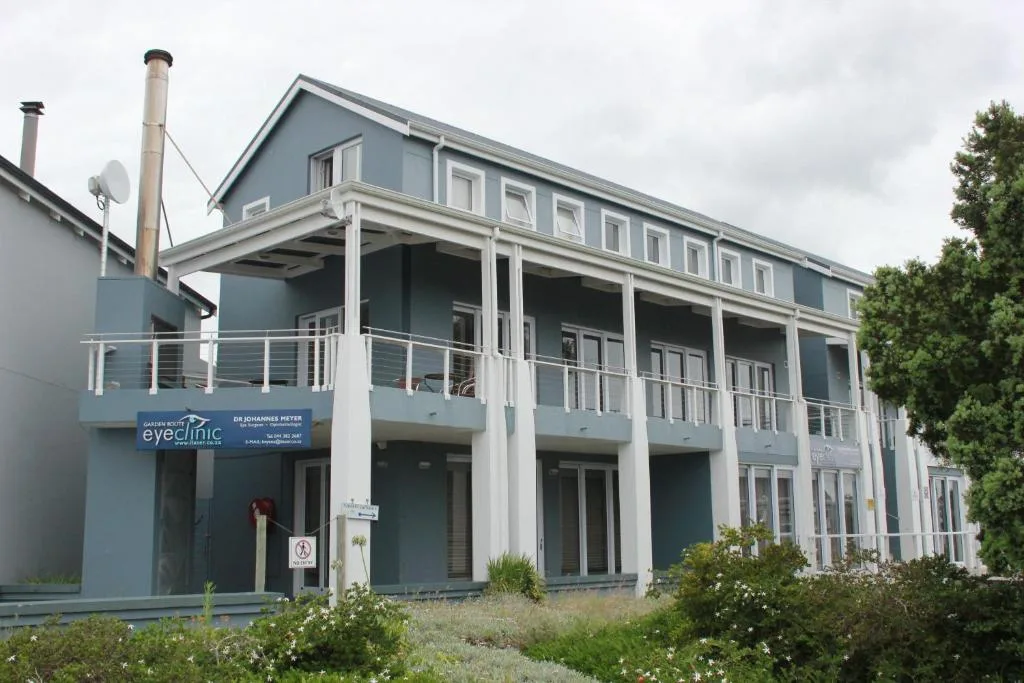 Modern blue and white building facade with covered deck and landscaped gardens